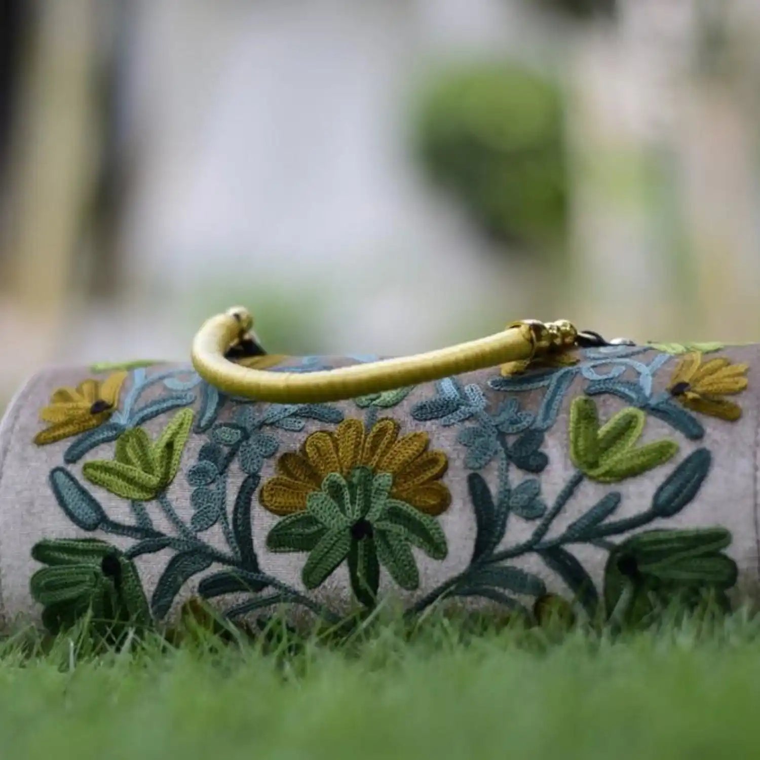 Embroidered cylindrical clutch bag with a golden handle.
