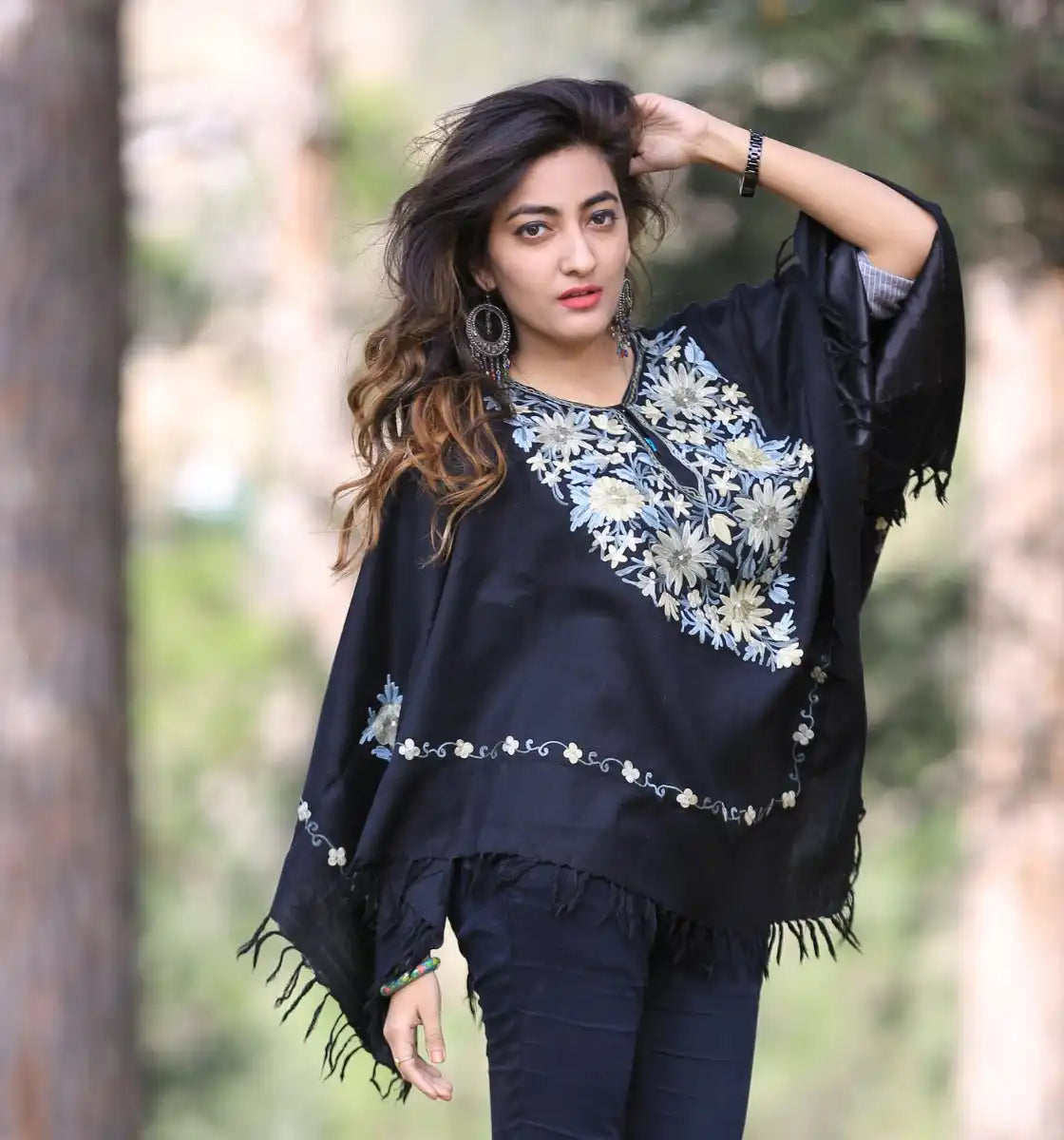 A woman modeling a black poncho with colorful floral embroidery and fringe trim.