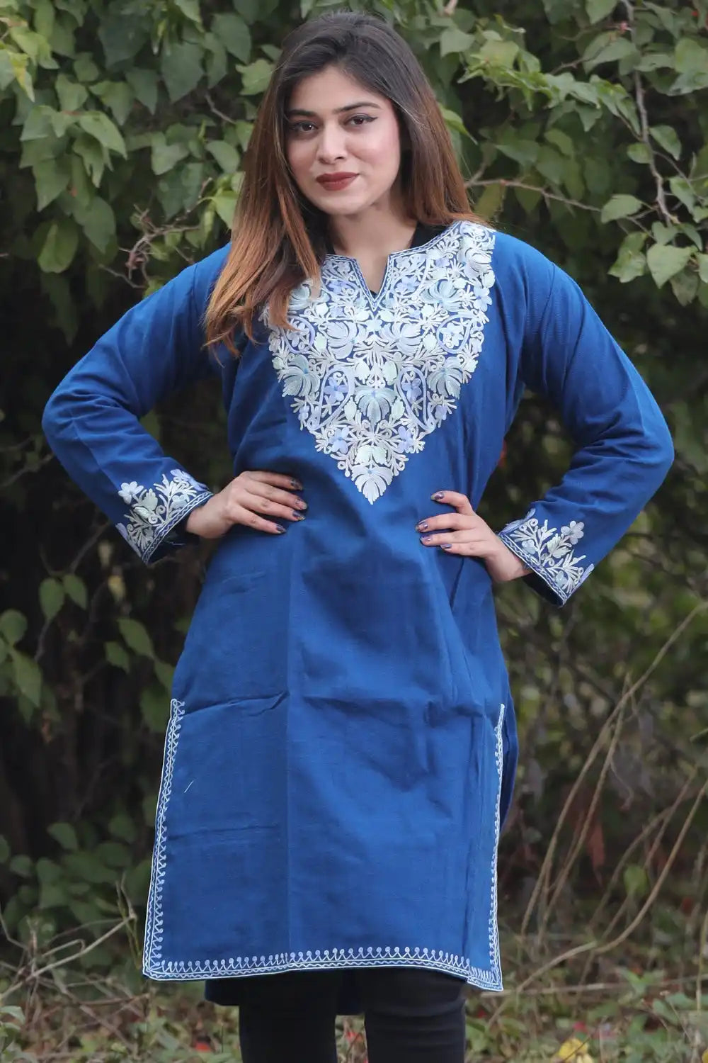 A woman wearing a blue embroidered kurti with black leggings.