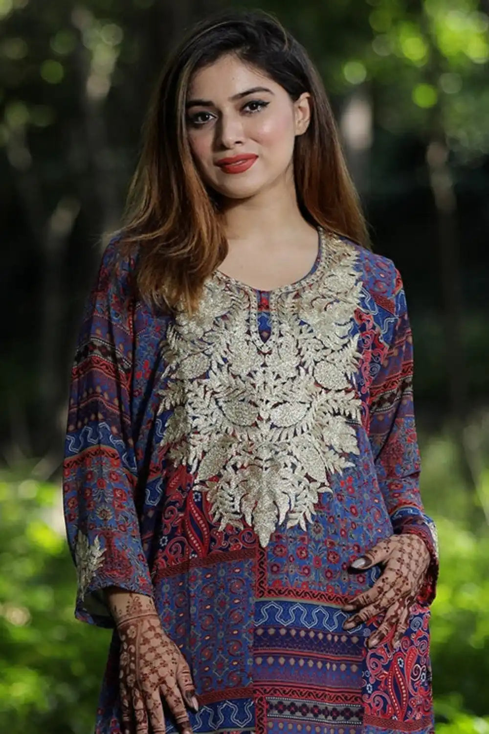 A woman modeling a colorful tunic with intricate embroidery and henna-decorated hands.
