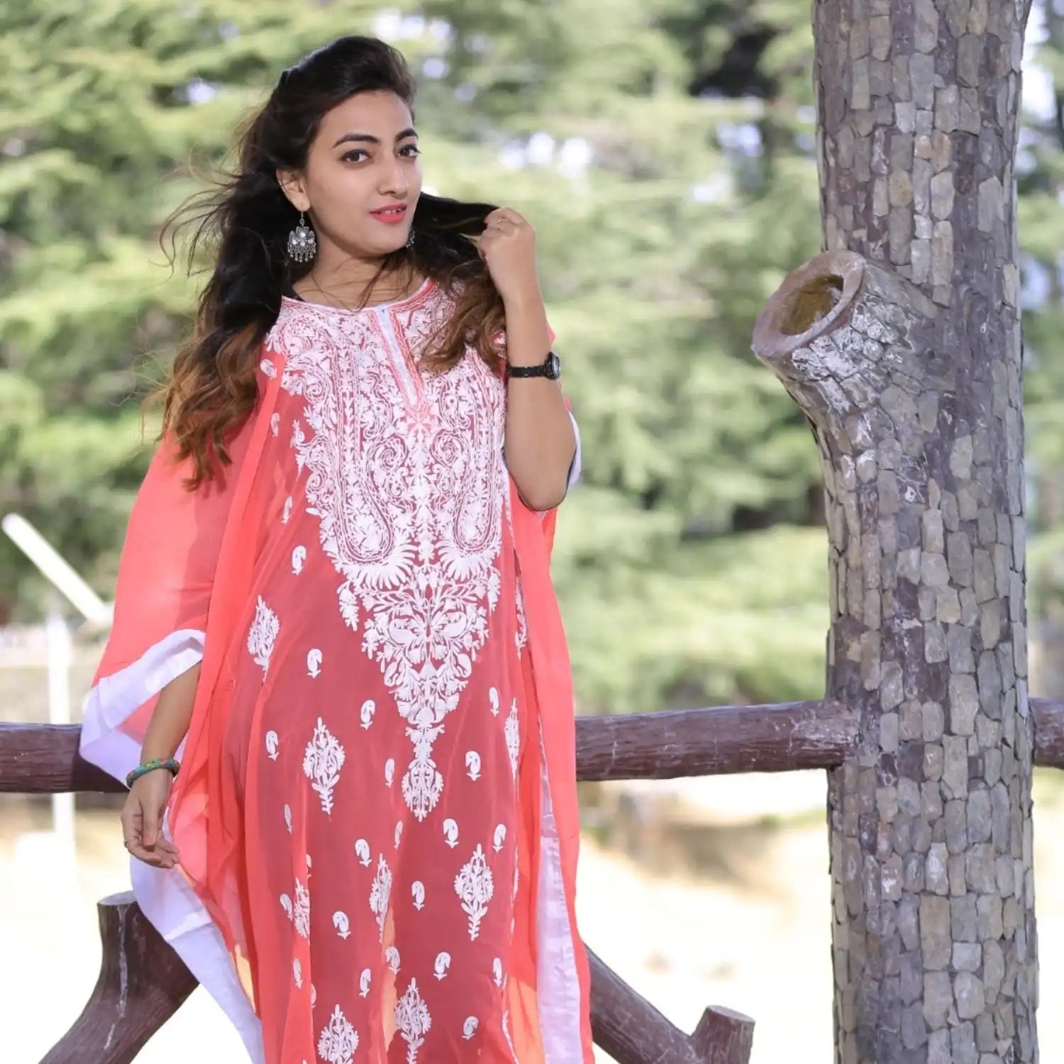 A woman in a flowing, coral-colored kaftan with intricate white embroidery.