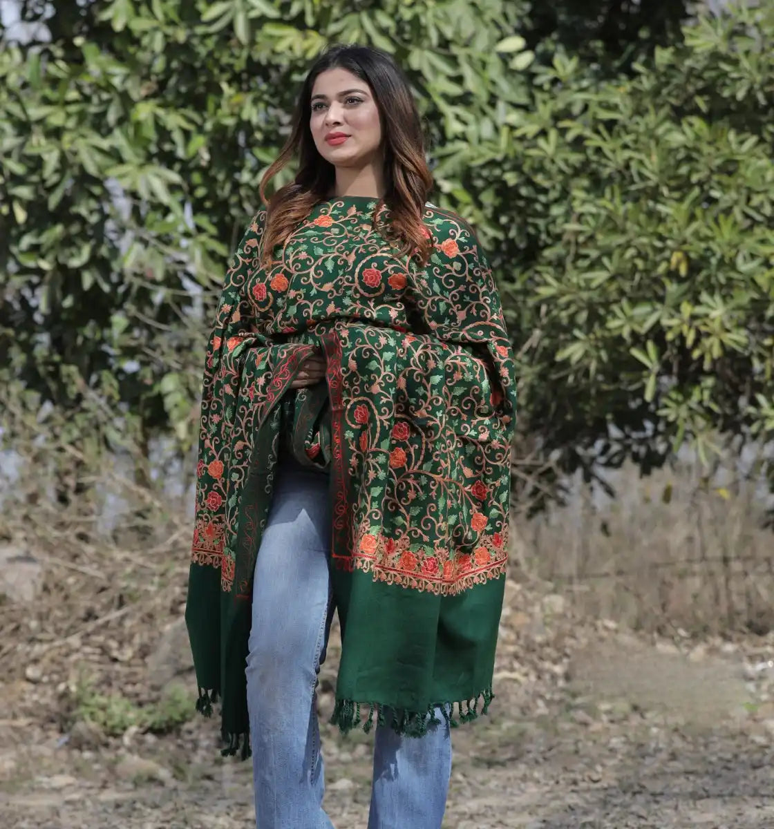 A woman wearing a dark green, intricately embroidered floral shawl over blue jeans.