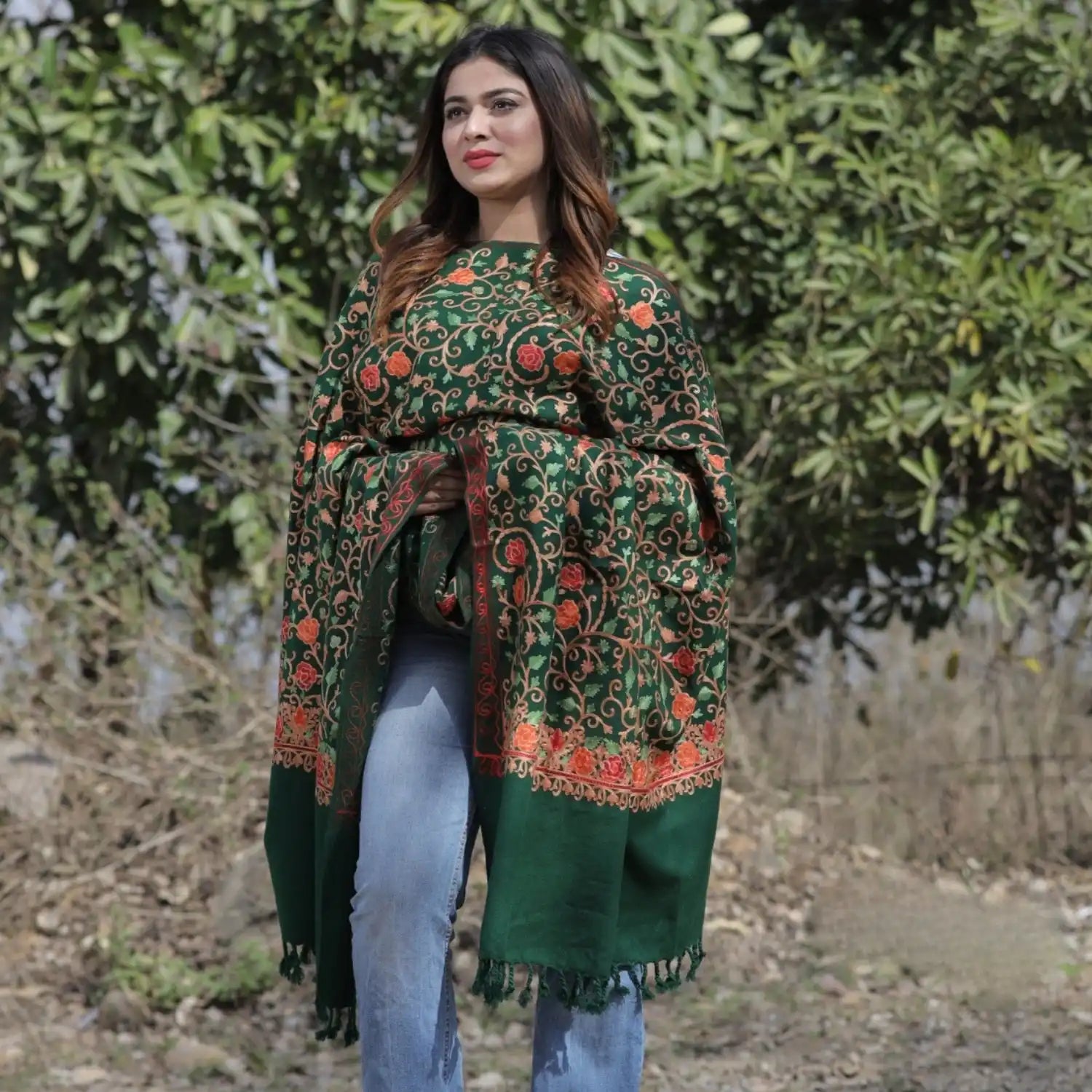 A woman wearing a dark green shawl with intricate orange and red floral embroidery.