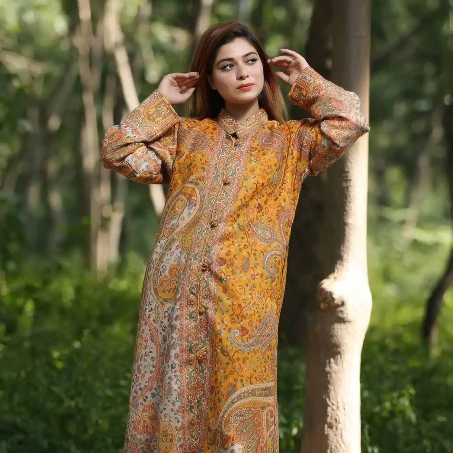 A woman wearing a long, loose-fitting, mustard yellow and multicolored paisley patterned dress or robe.