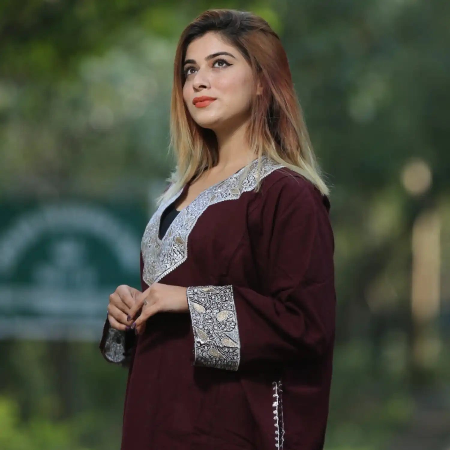 A woman wearing a maroon traditional tunic with intricate silver embroidery.