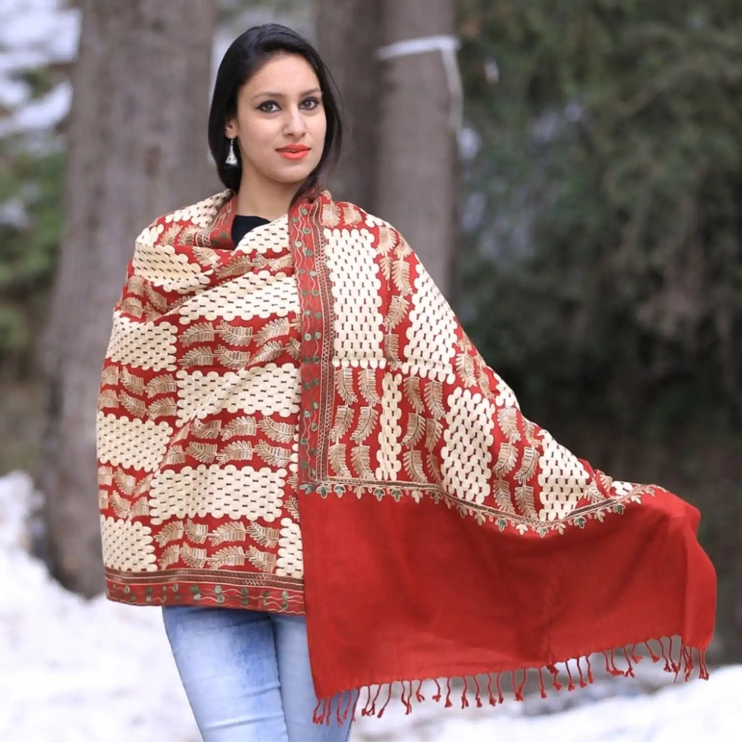 A woman modeling a red and off-white patterned shawl with tassels.
