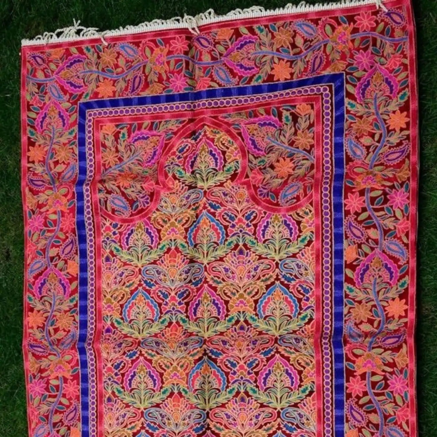 A vibrant, intricately embroidered prayer rug with floral and paisley patterns and a decorative border.
