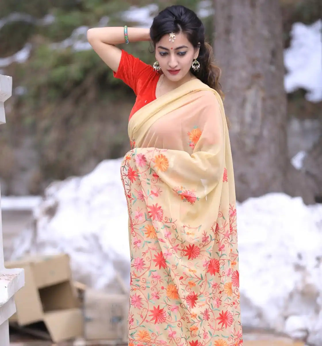 A woman wearing a light yellow saree with colorful floral embroidery and a red blouse.